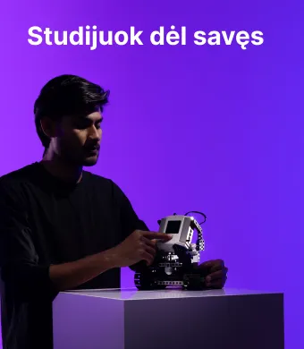 Studijuok dėl savęs Elektros ir elektronikos fakultete KTU. Jaunas tarptautinis studentas susikaupęs dirba su nedideliu robotikos įrenginiu, stovinčiu ant balto stalo, ryškiame violetiniame fone.